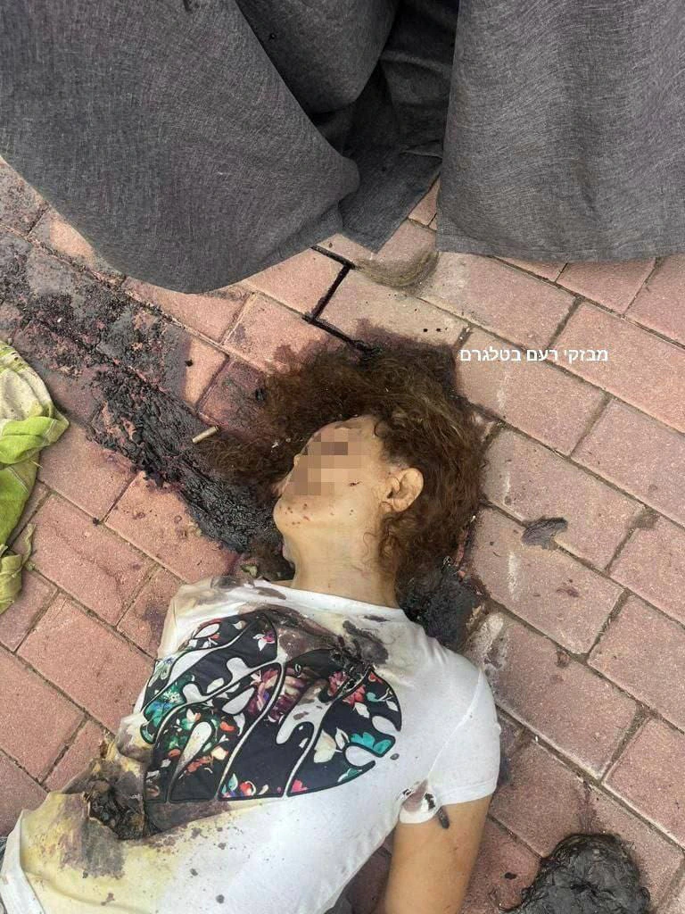 גופת אישה צעירה עם שיער מתולתל, פניה מטושטשות, שרועה על אבני מדרכה עם סימני שריפה