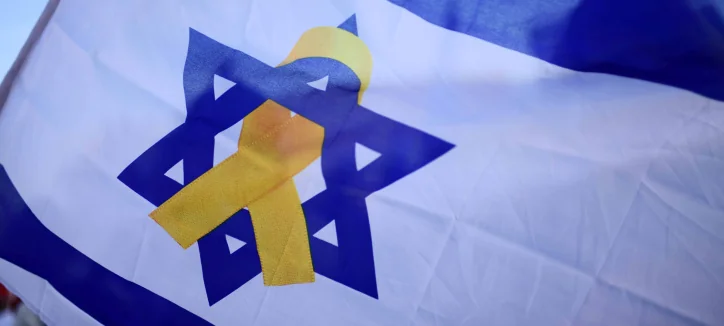 דגל ישראל מתנופף ברוח, ועליו סרט צהוב המונח על מגן הדוד שבמרכזו