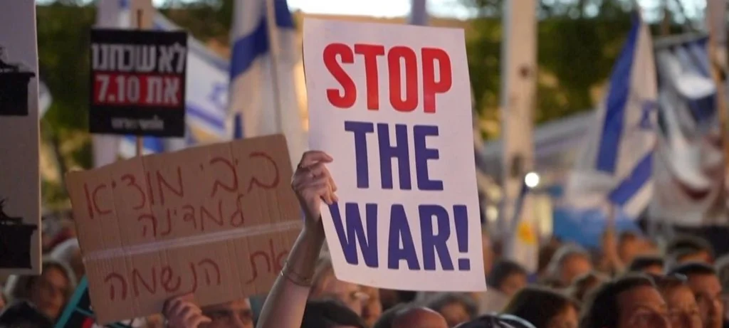 מפגינים מניפים שלטים בעברית ובאנגלית, ובהם "STOP THE WAR!", לצד דגלי ישראל