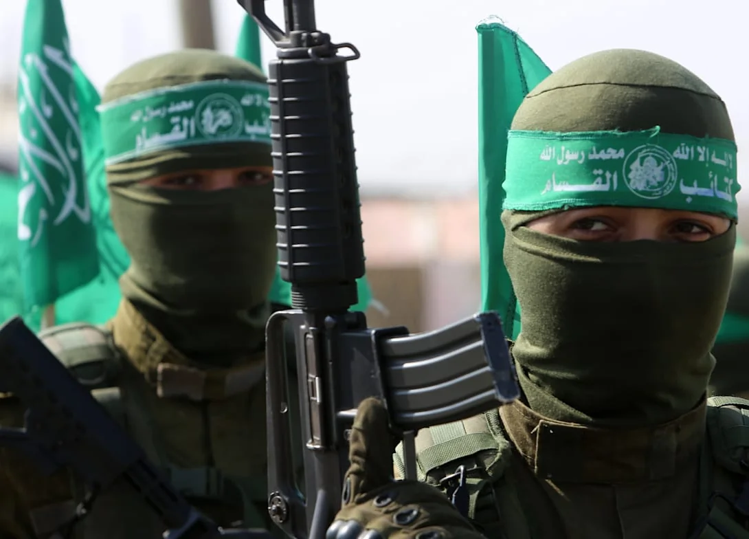 שני מחבלים רעולי פנים עם סרטי ראש ירוקים של גדודי עז א-דין אל-קסאם, רובה ודגלי חמאס ברקע
